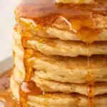 Stack of fluffy pancakes with syrup and butter on a white plate
