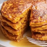 Stack of sweet potato pancakes with syrup and fork on a breakfast plate