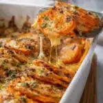 Garlic butter sweet potato bake with melted cheese and herbs in white dish