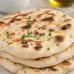 Stack of golden Greek yogurt naan with herbs on marble surface