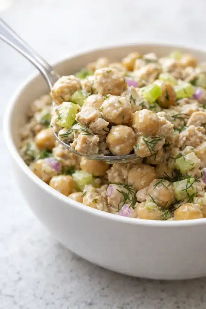 Spoon lifting creamy tuna garbanzo bean salad with celery and dill