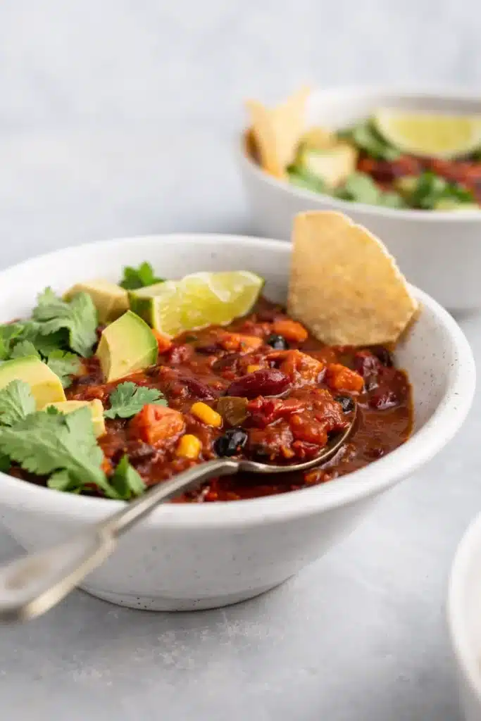 Close-up bowl of vegetarian chili with avocado, lime, and tortilla chip