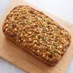 High protein cottage cheese oatmeal bread loaf on wooden board topped with oats and seeds