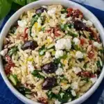 Mediterranean orzo pasta salad with feta, sun-dried tomatoes, and olives in a white bowl