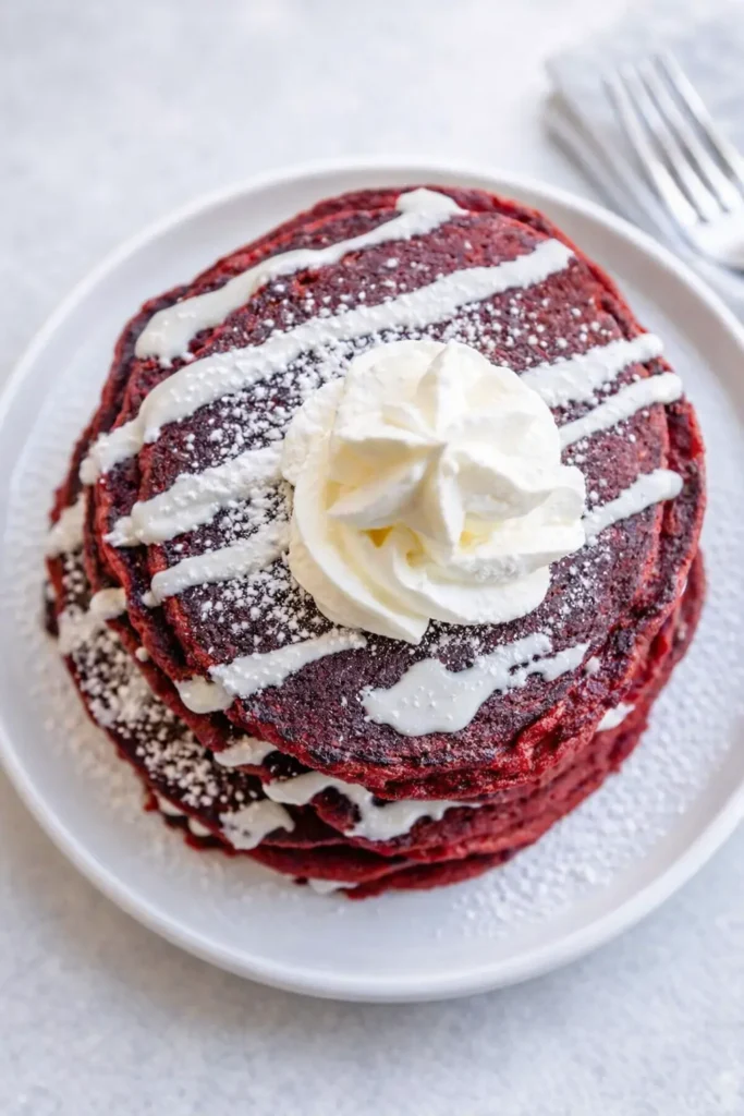 Stack of IHOP red velvet pancakes with cream cheese glaze and whipped cream on white plate