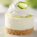 Mini key lime cheesecake with whipped cream and lime garnish on white plate