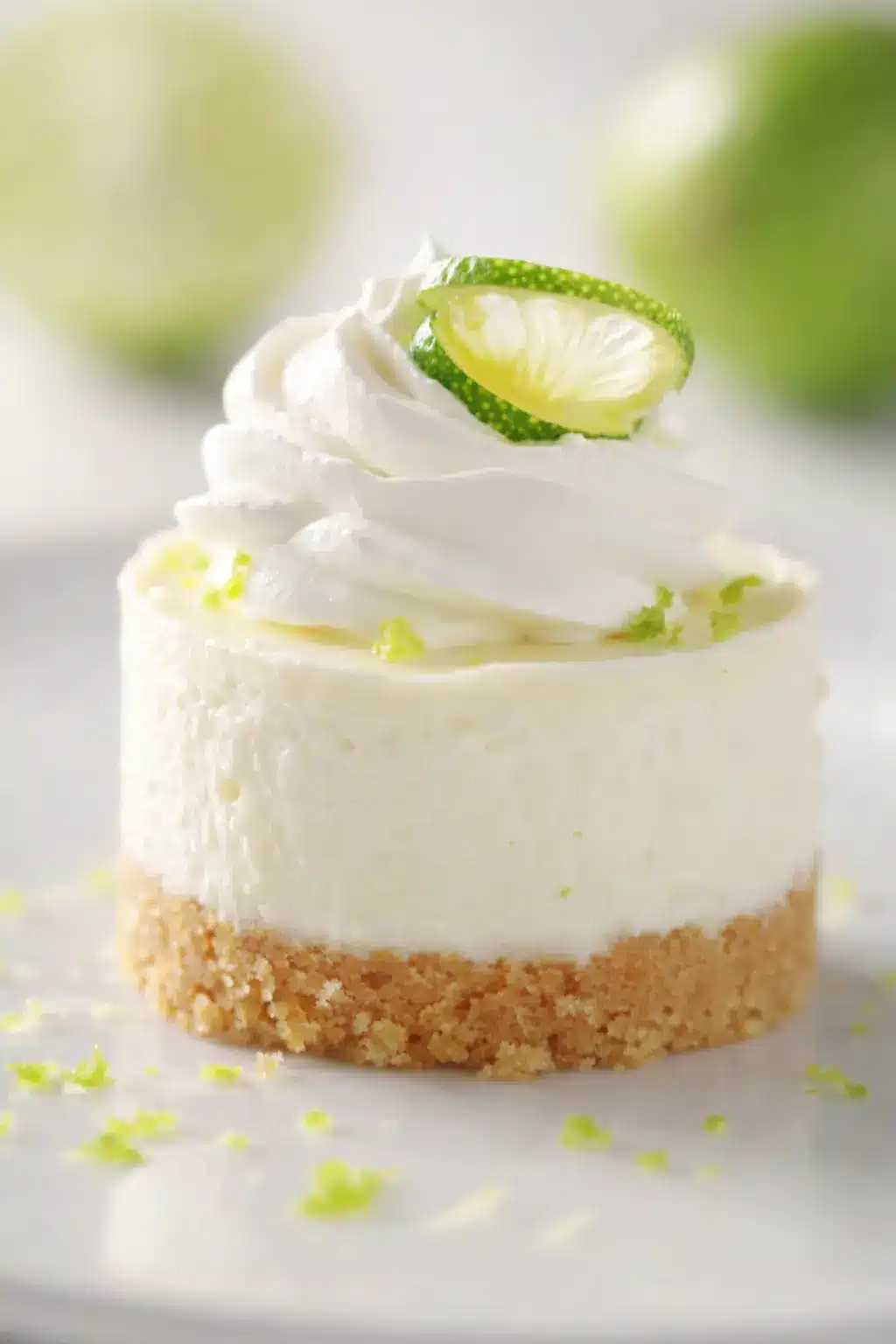 Mini key lime cheesecake with whipped cream and lime garnish on white plate