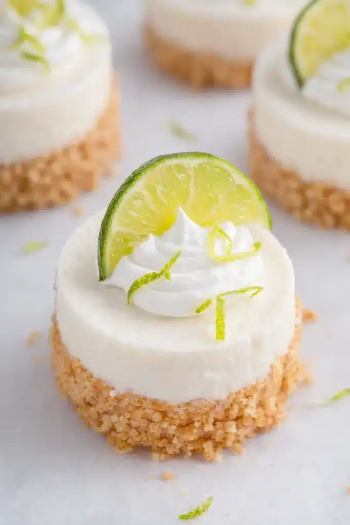 Mini Key Lime Cheesecakes | Amazing, Creamy, Tangy Treat 5 Mini key lime cheesecakes topped with whipped cream and lime slices on marble surface