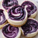 Mini lemon blueberry cheesecakes with graham crust and blueberry swirl on white plate