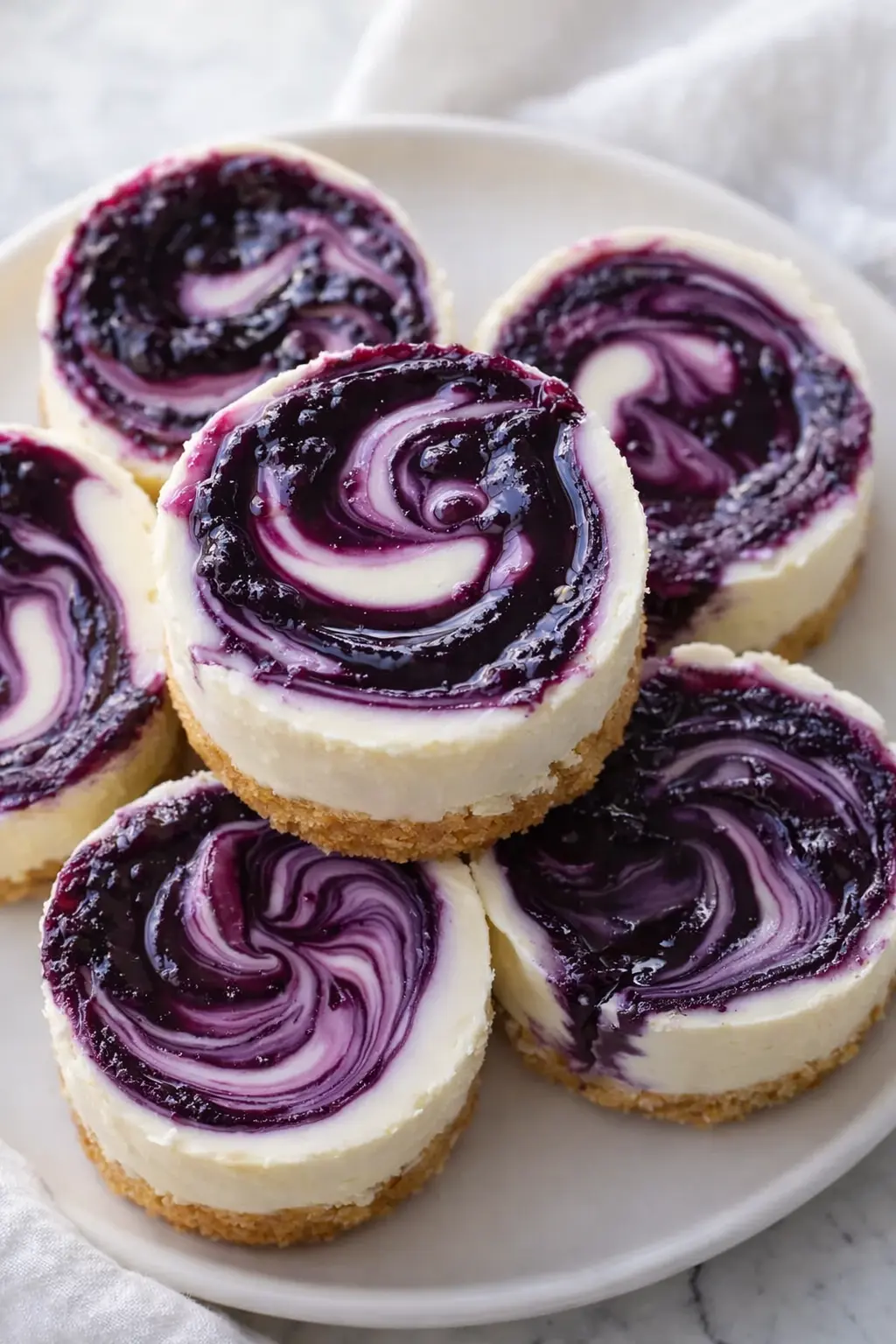 Mini lemon blueberry cheesecakes with graham crust and blueberry swirl on white plate