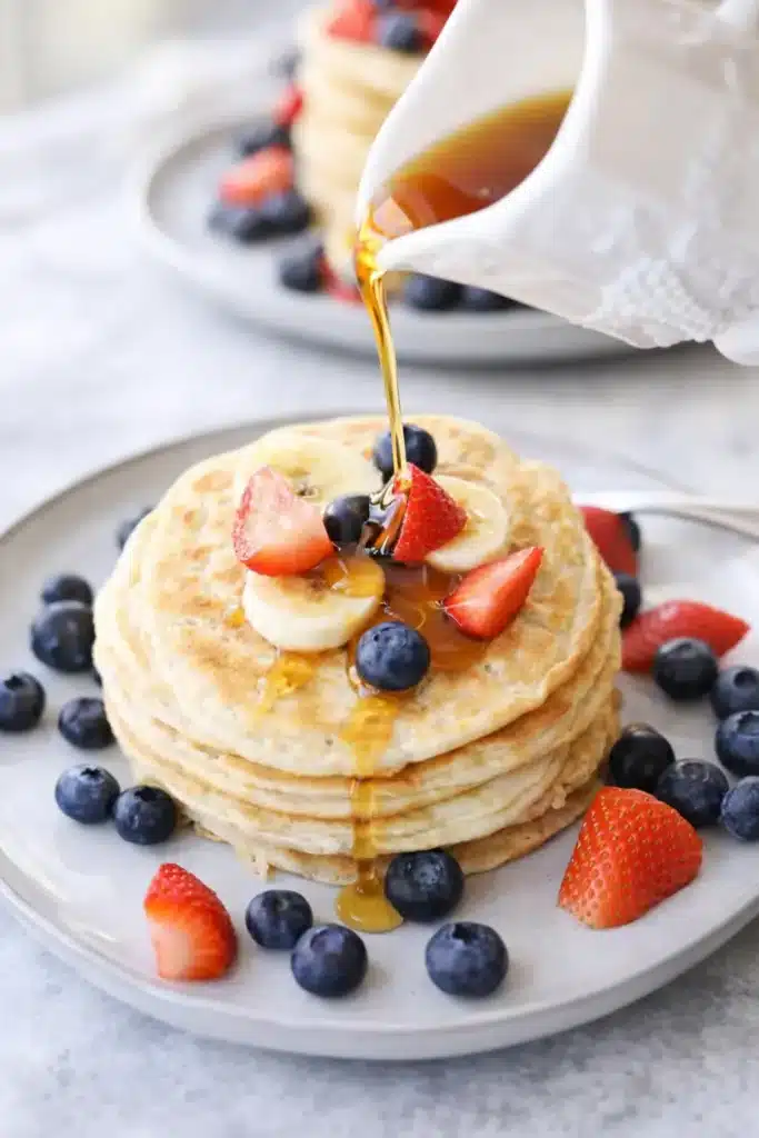 Protein pancakes topped with fruit and syrup on a white plate