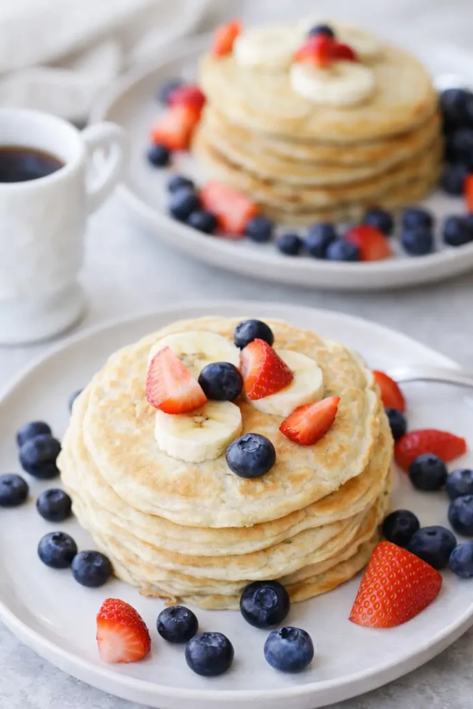 Golden protein pancakes with banana, blueberries, and strawberries on a white plate
