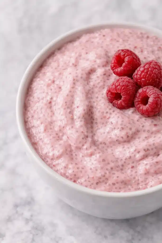 Raspberry chia seed pudding topped with fresh raspberries in a white bowl