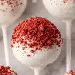 Red velvet cake pops coated in white chocolate with red cake crumb topping
