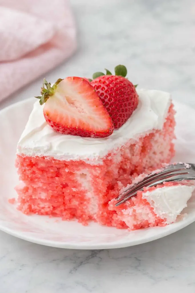 Strawberry Jello Poke Cake | Easy, Refreshing, and Delicious 6 Strawberry Jello poke cake slice with whipped cream and strawberries on marble background