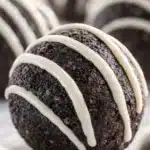 Chocolate Oreo protein ball with white chocolate drizzle on light surface