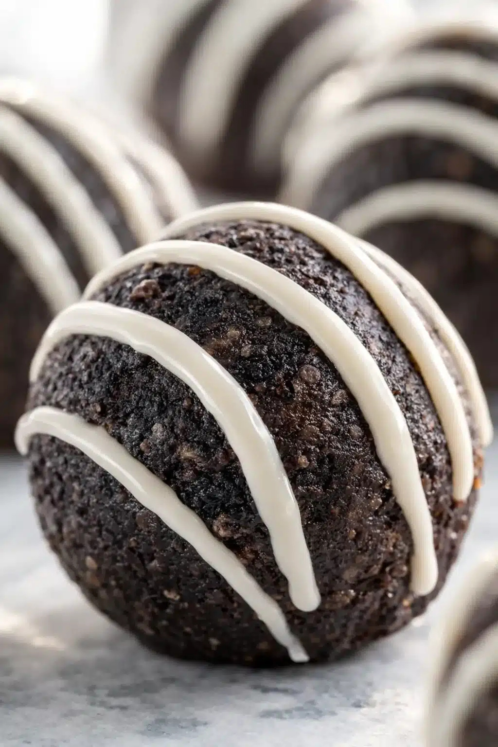 Chocolate Oreo protein ball with white chocolate drizzle on light surface