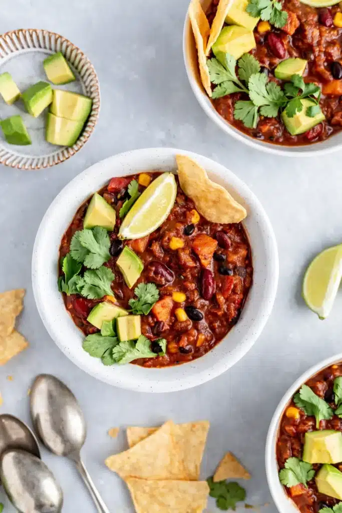 Overhead view of vegetarian chili bowls with avocado, lime, and tortilla chips