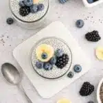 Vanilla chia pudding with banana, blueberries, and blackberries in glass jars on a light surface