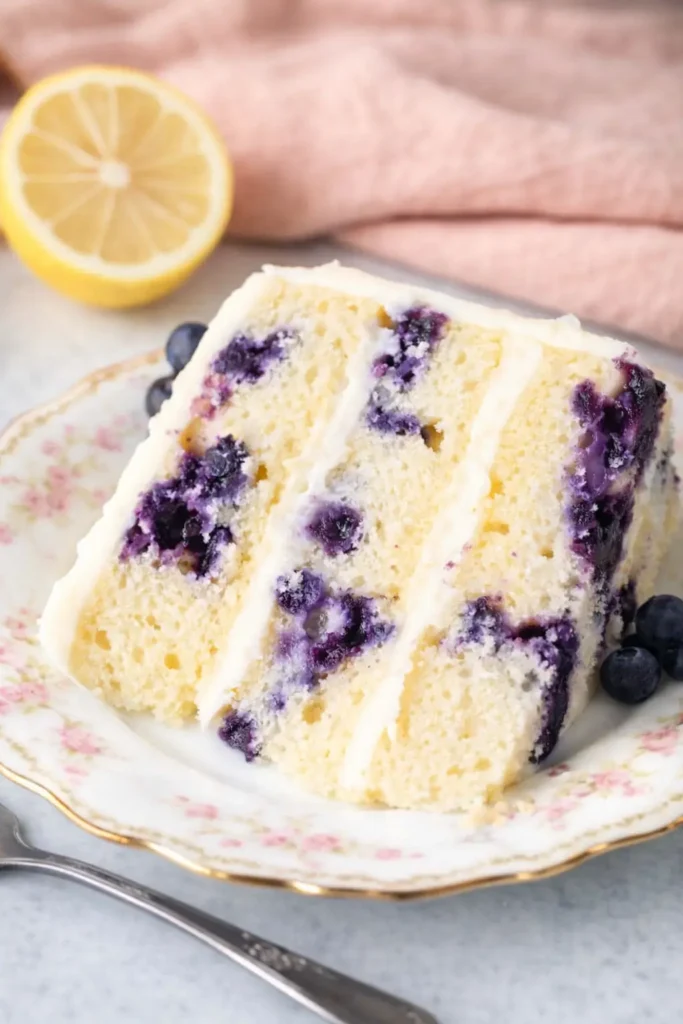 Slice of lemon blueberry layer cake with cream cheese frosting on vintage plate