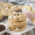 Chewy Cadbury egg cookies stacked with pastel mini eggs on a baking surface
