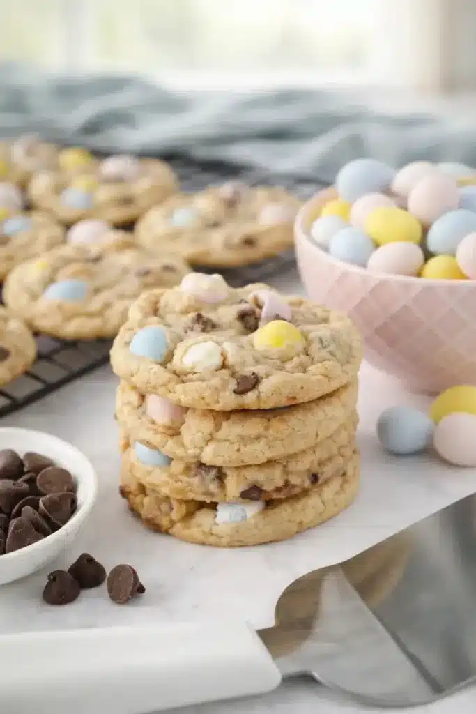 Chewy Cadbury egg cookies stacked with pastel mini eggs on a baking surface