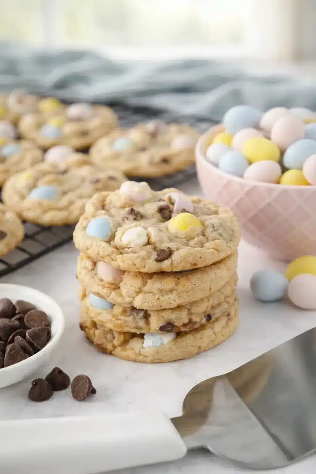 Chewy Cadbury egg cookies stacked with pastel mini eggs on a baking surface