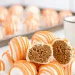 Carrot Cake Cheesecake Bites coated in white chocolate with orange drizzle on a plate