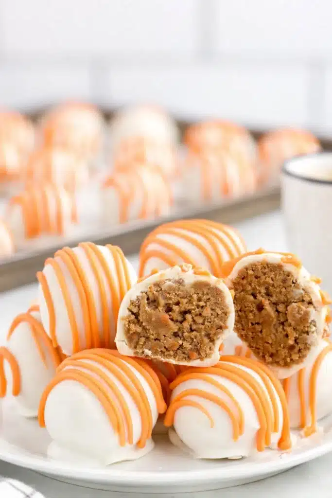 Carrot Cake Cheesecake Bites coated in white chocolate with orange drizzle on a plate