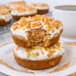 Stacked carrot cake donuts with cream cheese frosting and walnuts on a plate