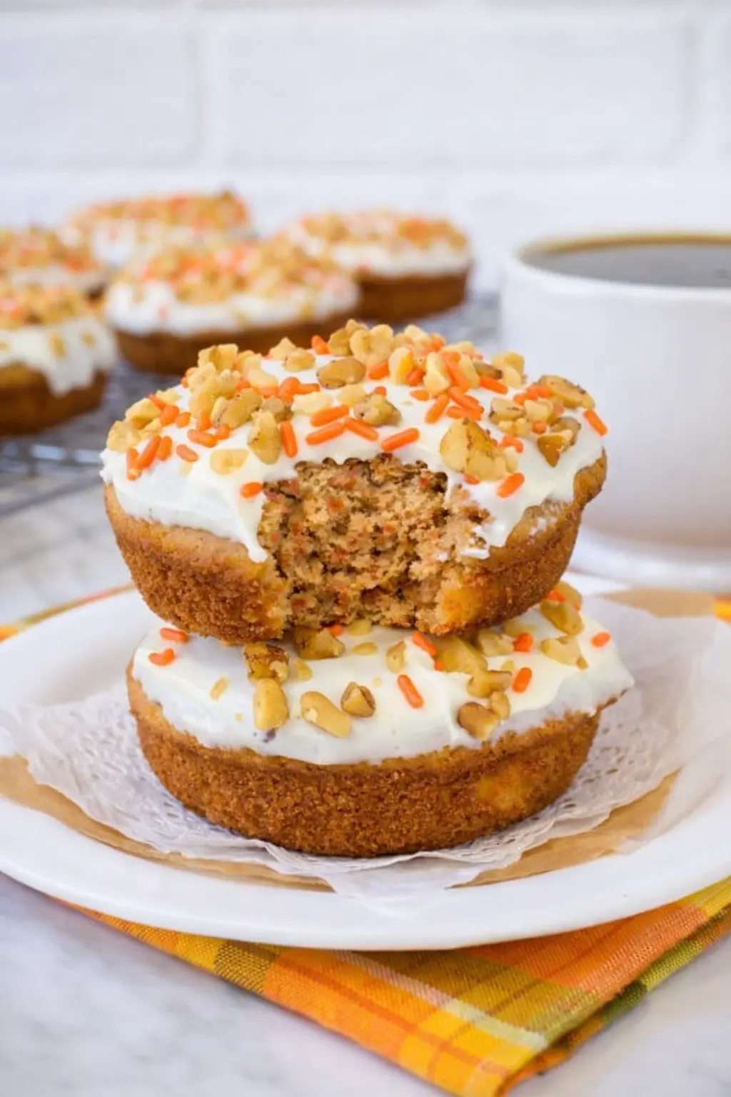 Stacked carrot cake donuts with cream cheese frosting and walnuts on a plate