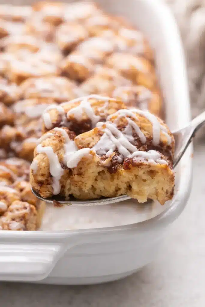  Spoon lifting soft Cinnamon Roll Casserole with vanilla glaze