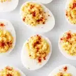 Classic deviled eggs with creamy yolk filling and paprika on white surface