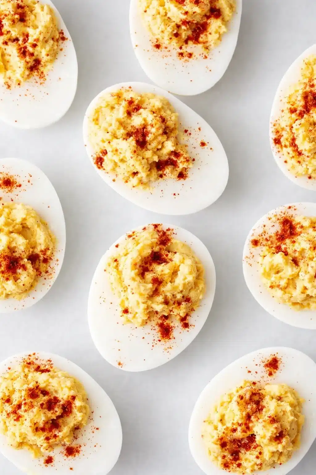 Classic deviled eggs with creamy yolk filling and paprika on white surface