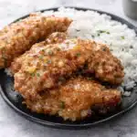 Crispy Bang Bang chicken with rice and sweet chili sauce on a black plate