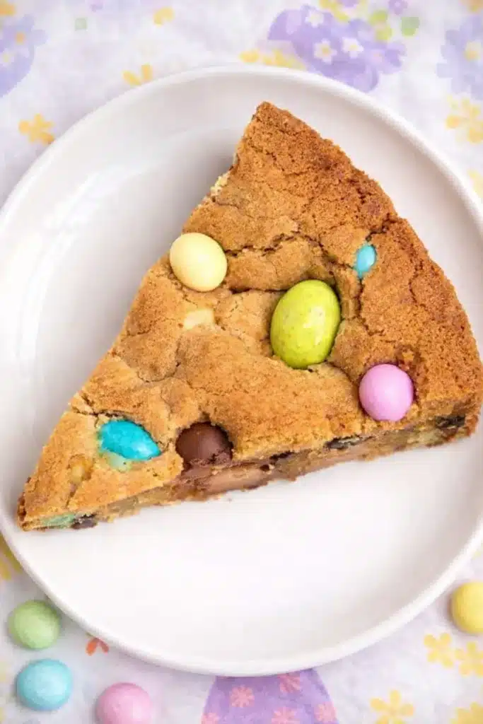 Slice of Easter cookie cake with pastel chocolate eggs on a white plate