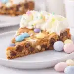Slice of Easter Cookie Cake with pastel candies and vanilla frosting on ceramic plate