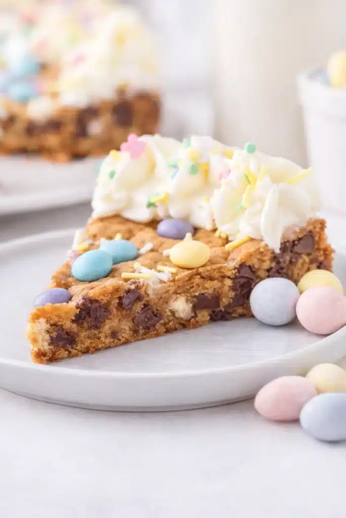 Slice of Easter Cookie Cake with pastel candies and vanilla frosting on ceramic plate