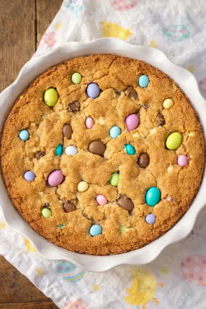 Easter cookie cake in white dish topped with colorful chocolate eggs