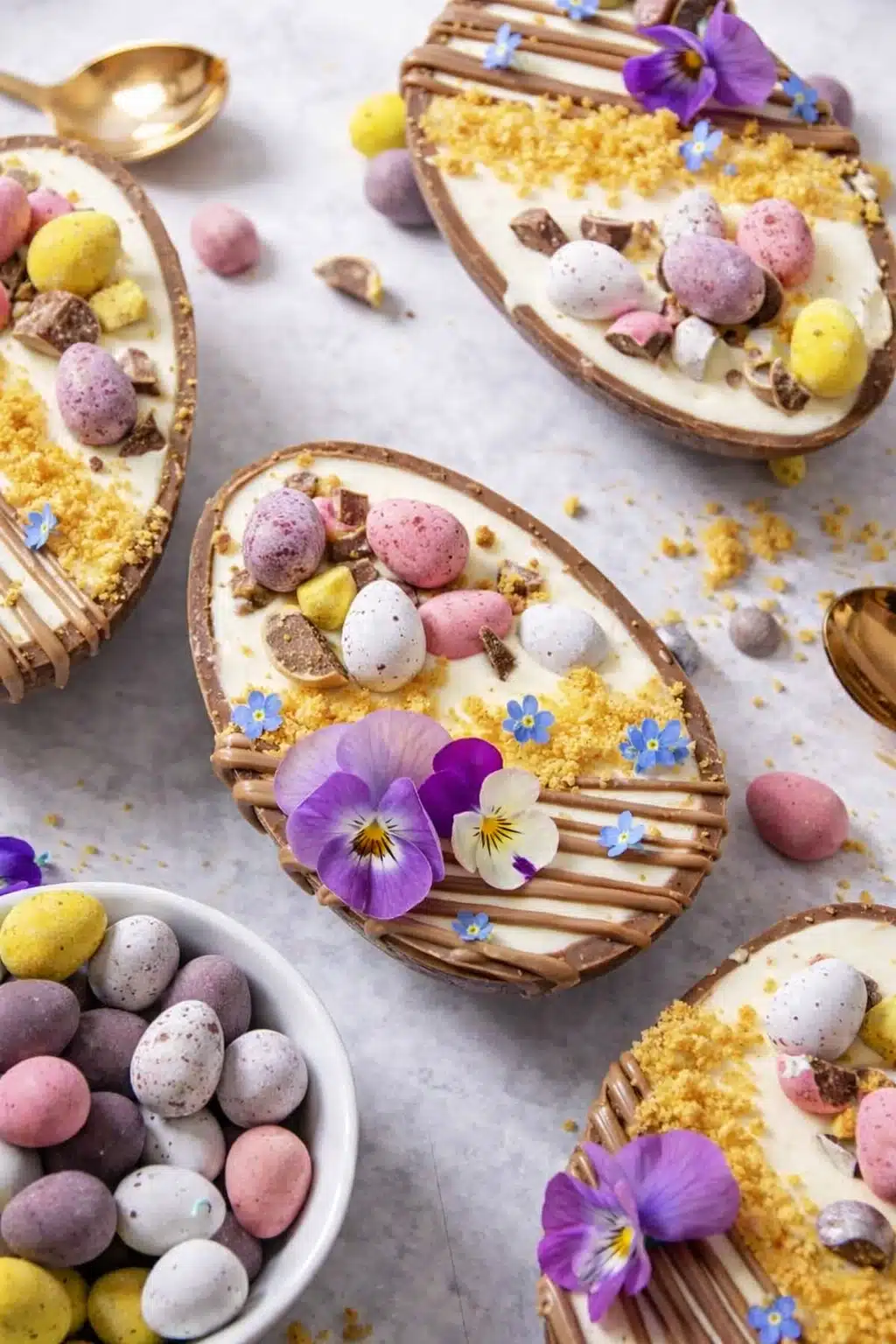 Easter egg cheesecakes with mini eggs and edible flowers on a light background