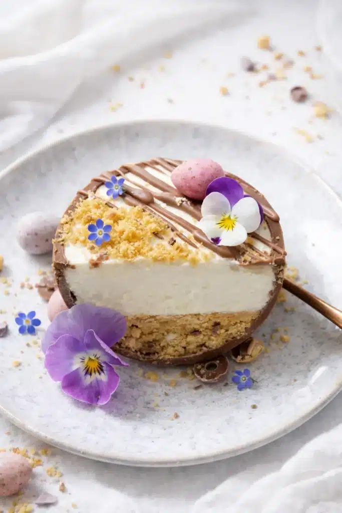 Slice of Easter Egg Cheesecake on plate with mini eggs and flowers