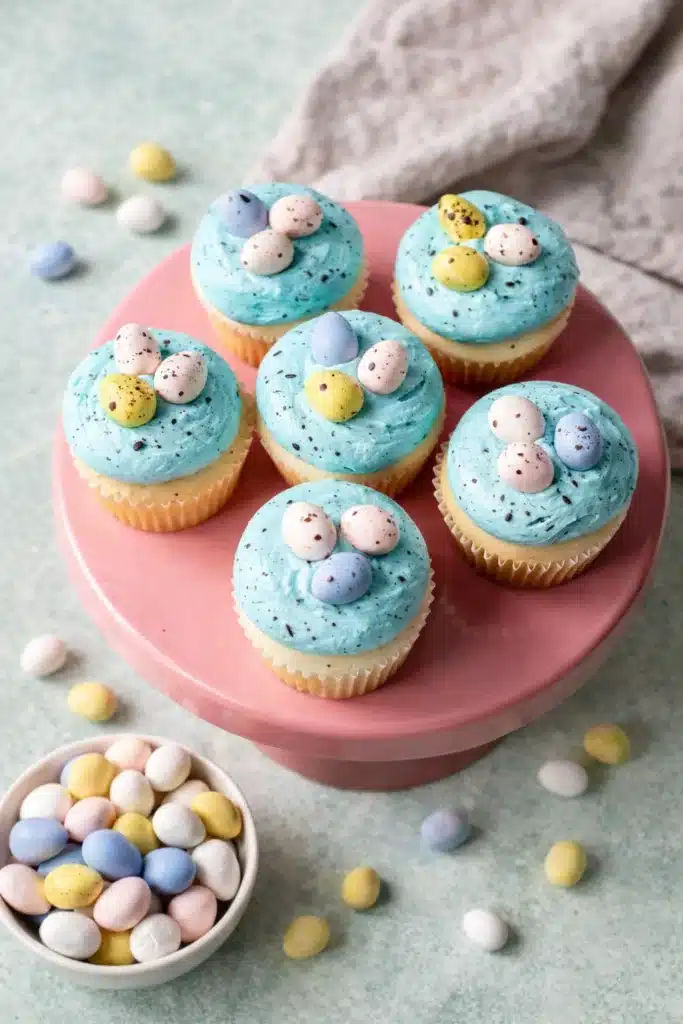 Egg Easter Cupcakes Easy Beautiful Easter Treat 12 Egg Easter Cupcakes with blue frosting and pastel mini eggs on pink stand