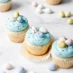 Egg Easter Cupcakes with blue frosting and pastel mini eggs on light stone surface