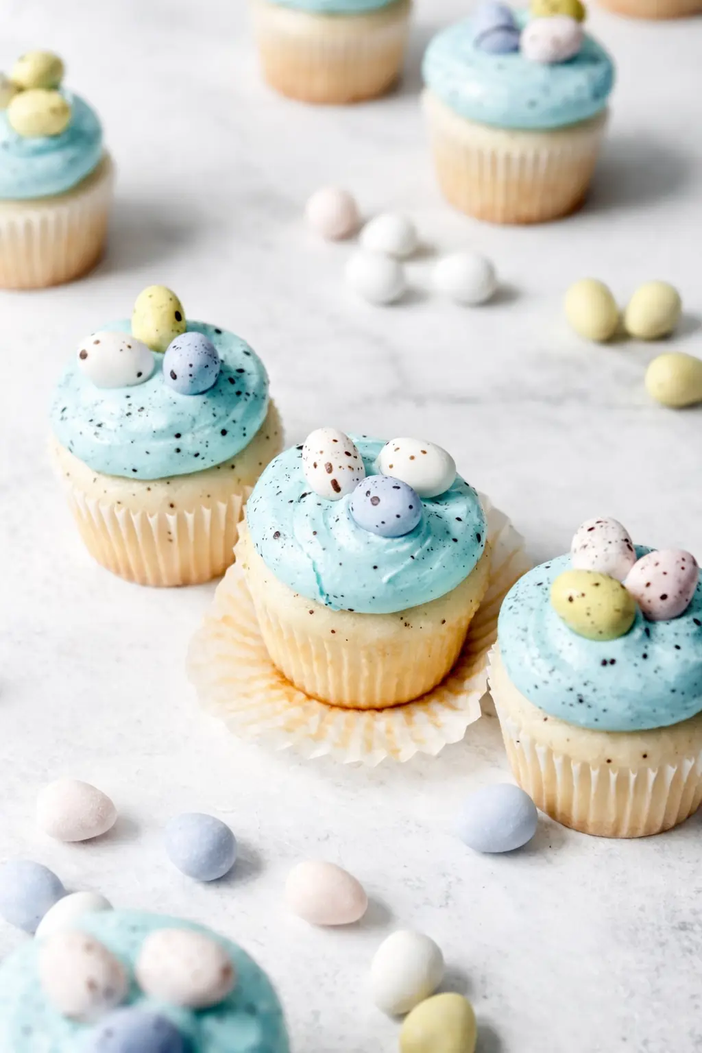 Egg Easter Cupcakes with blue frosting and pastel mini eggs on light stone surface