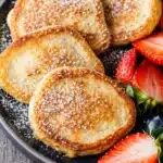 Golden cottage cheese pancakes with powdered sugar and fresh berries on dark plate