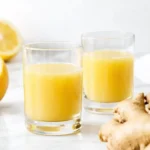 Two glasses of fresh ginger shots with lemon and ginger root on a bright countertop