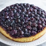 Homemade blueberry upside down cake with glossy caramelized topping on a white plate