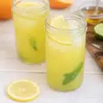 Homemade electrolyte drink with lemon, mint, and ice in glass jars on marble surface