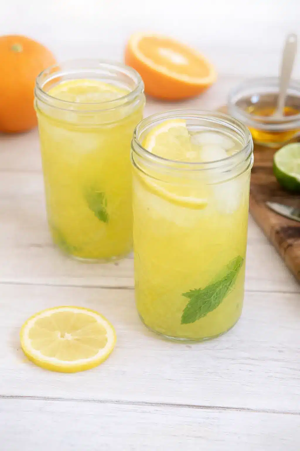 Homemade electrolyte drink with lemon, mint, and ice in glass jars on marble surface