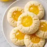 Homemade lemon curd thumbprint cookies on a plate with glossy lemon filling